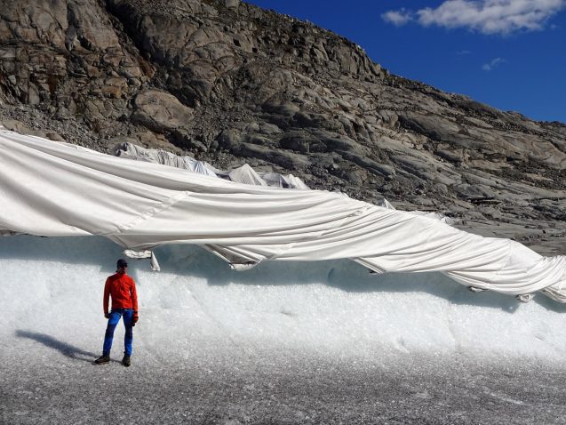 A researcher stands in front of the Rhone Glacier covered in geotextiles to protect it from accelerated melting. © Matthias Huss
